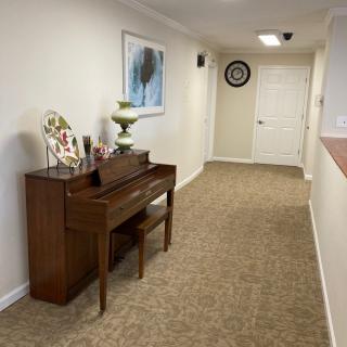 A cozy hallway featuring a small piano with a bench, adorned with decorative items and artwork on the wall.