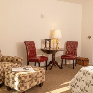 A cozy living room setup with patterned armchairs, red upholstered chairs, a wooden table, and a lamp.