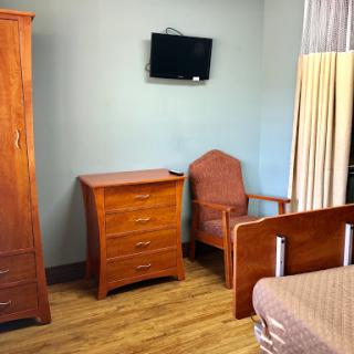 A cozy room featuring wooden furniture, including a bed, wardrobe, and chair, with a television mounted on the wall.