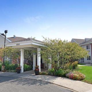 A landscaped entrance to a large building with a driveway and greenery.