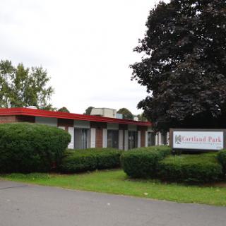 A building with a prominent sign, surrounded by greenery and under a cloudy sky.