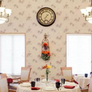 A beautifully set dining room with a central table, decorative wall clock, and floral arrangements.