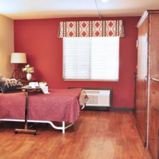A cozy bedroom with red walls, a bed, wardrobe, and a lamp near the window.