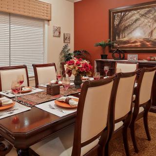 A well-decorated dining room featuring a polished wooden table set for a meal, surrounded by elegant chairs and accented with flowers and artwork.