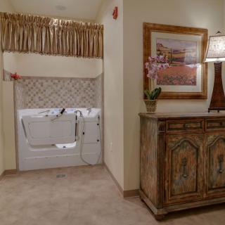 A cozy bathroom interior featuring a walk-in bathtub, decorative furniture, and wall art.