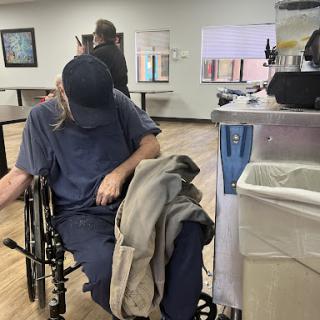 A person seated in a wheelchair, dressed casually, in what appears to be a medical facility.