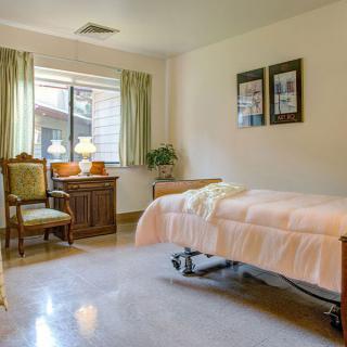 A cozy room with a hospital bed, armchair, and a window view.