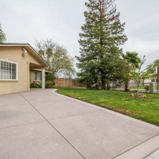 A suburban house with a concrete driveway and a grassy yard surrounded by trees.