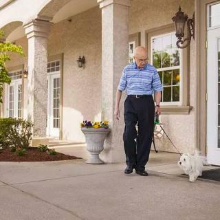 An elderly person walking a small dog in front of a building with columns.