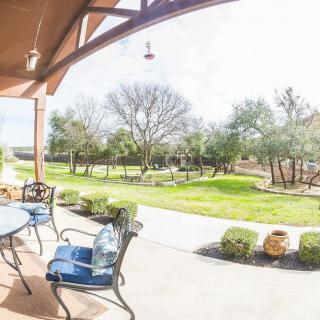 A sunny patio with seating overlooking a lush garden and lawn.