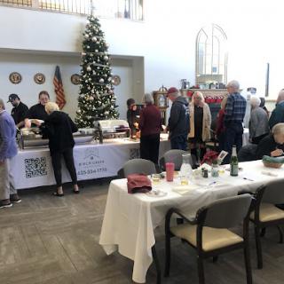A festive gathering with a Christmas tree, where guests line up to enjoy a meal together.