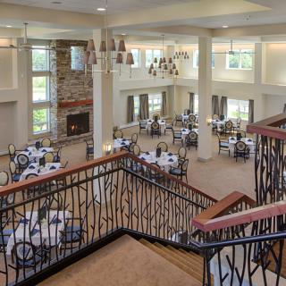 A spacious dining hall with elegant chandeliers and a grand staircase, featuring several tables set for guests.