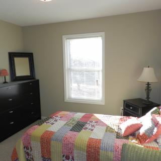 A cozy bedroom with a colorful quilt on the bed, a dresser with a mirror, and a window letting in natural light.