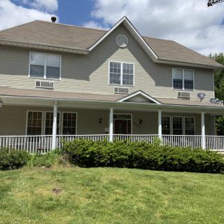 A two-story suburban house with a large porch and a green lawn on a cloudy day.