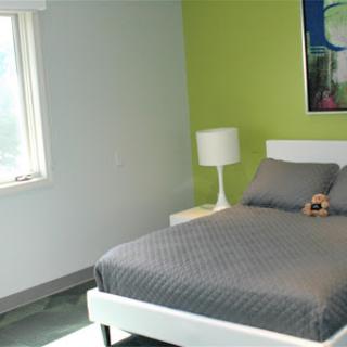 A minimalist bedroom featuring a green accent wall and modern furnishings.