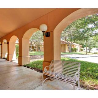 A covered walkway with arches, featuring a metal bench and surrounded by greenery.