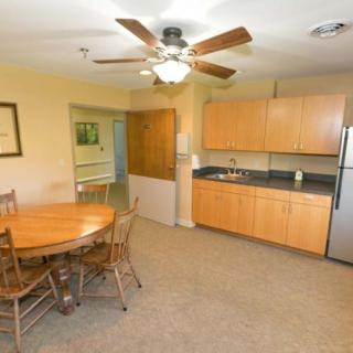 A cozy kitchen and dining area with wooden cabinets, a ceiling fan, and a round table with chairs.