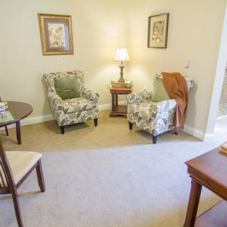 A cozy living room with two patterned chairs, a small wooden table, and a lamp.