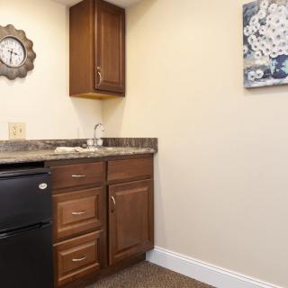 A small kitchenette area with a sink, brown cabinets, and a clock on the wall.