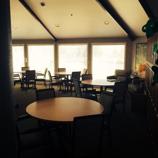 A sunlit room with tables and chairs arranged near large windows.