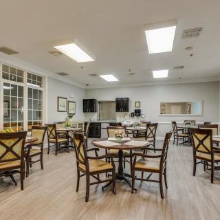 A spacious dining area with multiple tables and chairs, featuring bright lighting and a wooden floor.