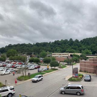 A view of a parking lot at a shopping center, surrounded by lush hills under a cloudy sky.