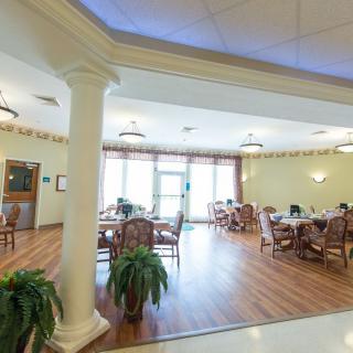 A spacious dining area with tables and chairs arranged neatly, featuring large windows and indoor plants.