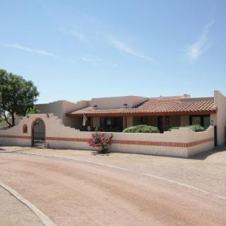 A single-story stucco house with a tile roof set in a desert landscape.