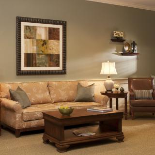 A cozy living room with a sofa, coffee table, and armchair, adorned with elegant wall art and warm lighting.
