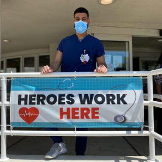 A healthcare worker stands proudly in front of a sign promoting the dedication and hard work of medical professionals.
