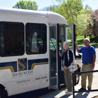 Two people boarding a small bus on a sunny day.