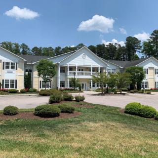 A large residential building surrounded by landscaped greenery under a clear blue sky.