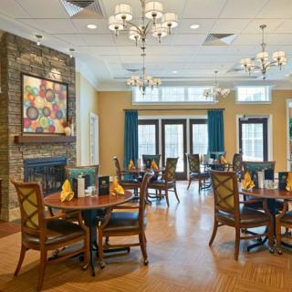 An elegant dining area featuring neatly arranged tables and chairs, with chandeliers and a fireplace enhancing the cozy atmosphere.