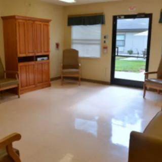 An empty waiting room with several chairs, a cabinet, and a view of the outside through a window and door.