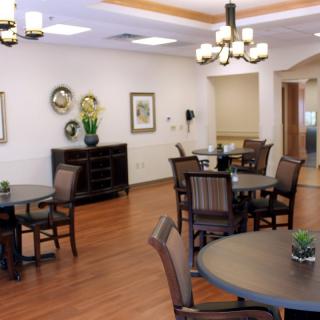 A cozy dining area with round tables and chairs, decorated with artwork and elegant lighting.