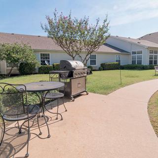 A sunny backyard patio featuring a grill and outdoor furniture.