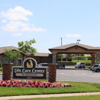 Entrance of a Life Care Center with a sign, landscaping, and parking area.