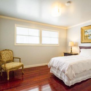 A cozy bedroom with a neatly made bed, an elegant chair, and warm wooden flooring.