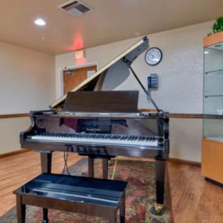 A grand piano with its lid open, set in a well-lit music room with wooden flooring.