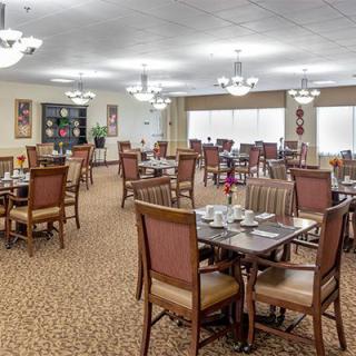 An empty dining room with neatly arranged tables and chairs, illuminated by elegant ceiling lamps.