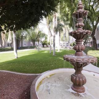 A tranquil garden with a classic tiered fountain amid lush greenery and trees.