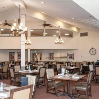 A spacious dining area with numerous tables and chairs, featuring ceiling fans and chandeliers.