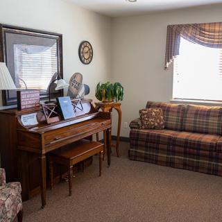 A cozy living room featuring a wooden piano, plaid couch, and decorative items.