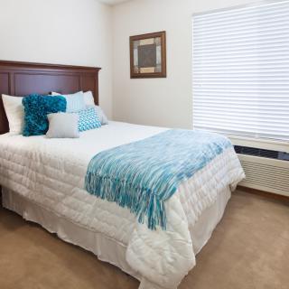 A neatly arranged bedroom featuring a bed with blue and white bedding near a window.