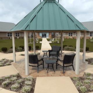 A gazebo surrounded by landscaping with chairs and a table, set beside a pathway.