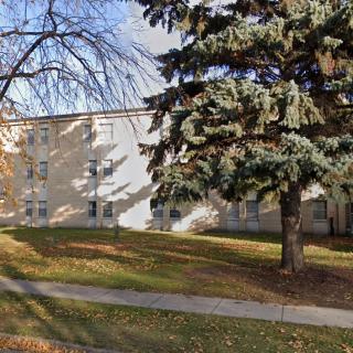 A residential building with a large tree and a sidewalk in the foreground on a sunny fall day.