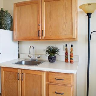 A compact kitchen area featuring wooden cabinets, a small sink, decorative items, and a floor lamp.