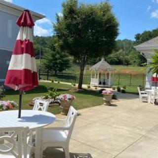 A sunny patio with chairs, a red and white umbrella, and a gazebo in a garden setting.