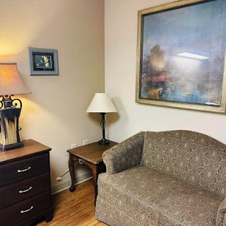 A cozy corner of a living room featuring a patterned couch, a lamp, and an artwork on the wall.