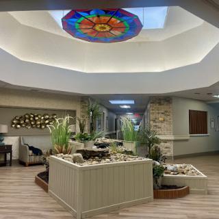 A serene and modern lobby featuring a stained glass ceiling, lush plants, and a calming water feature.